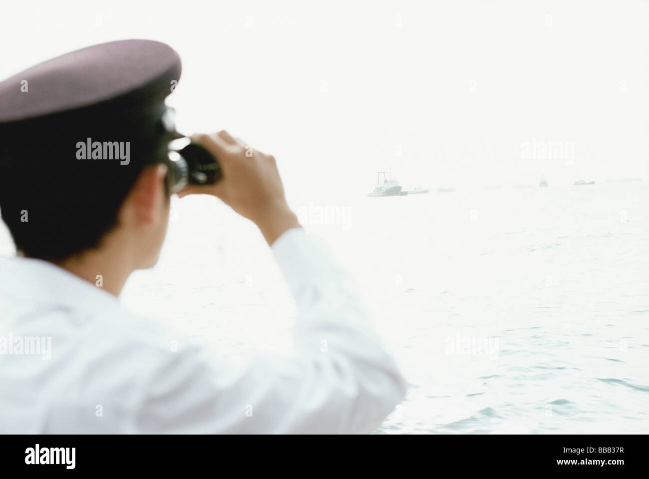 Homme en blanc avec des jumelles, regardant la mer Banque D'Images