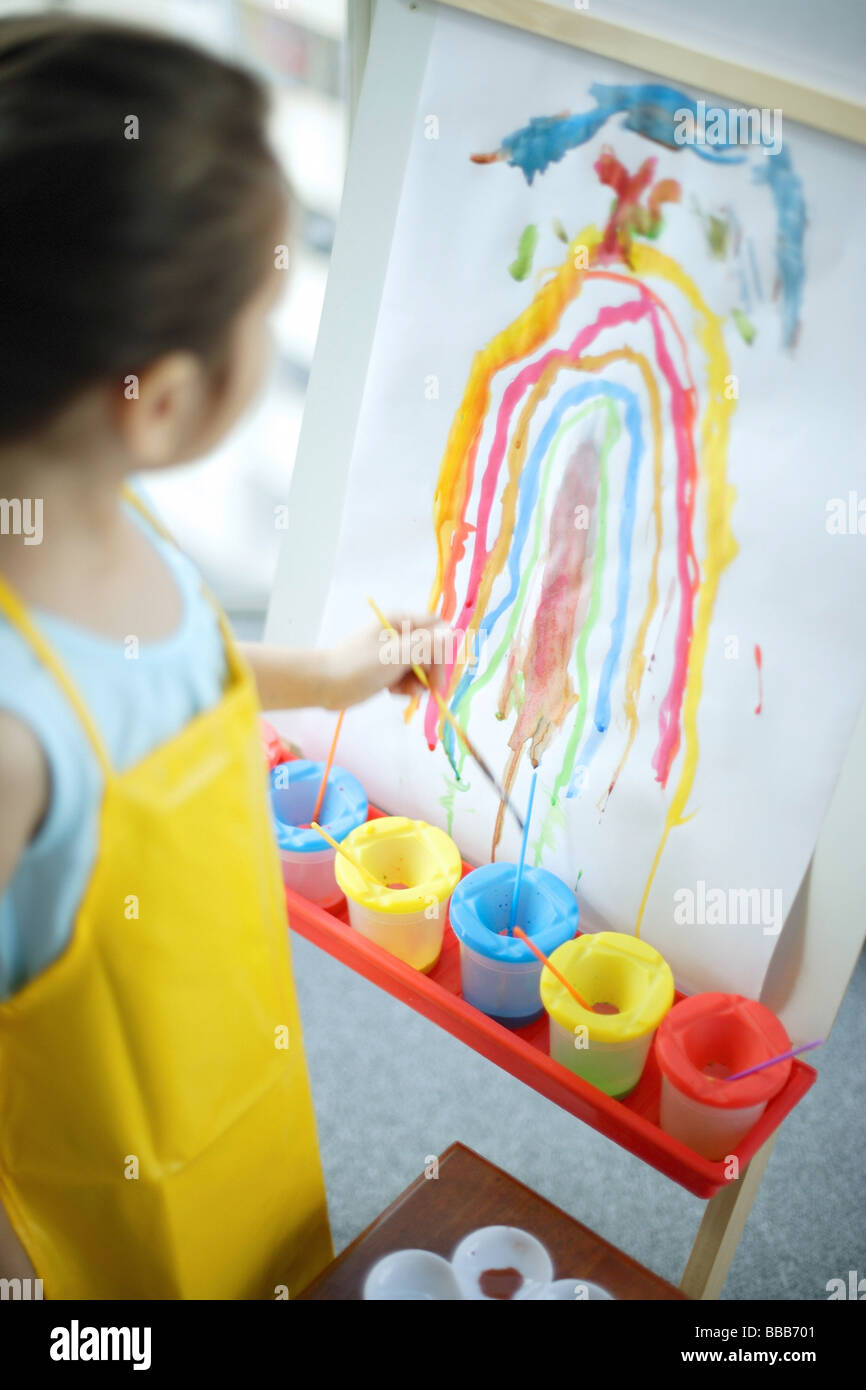 Young Girl standing in front of rainbow painting on easel Banque D'Images