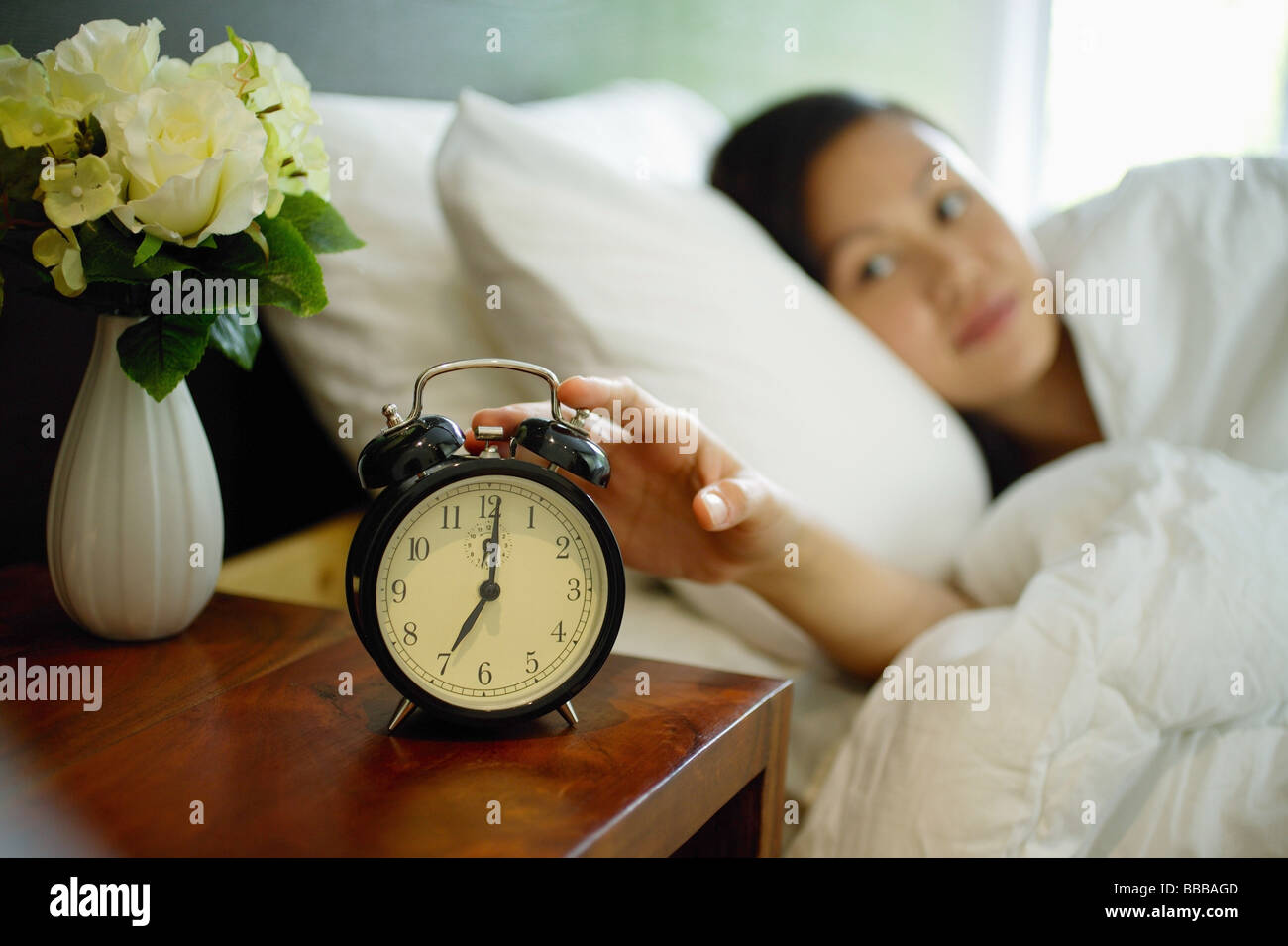 Femme au lit, vers de réveil sur la table de chevet Banque D'Images