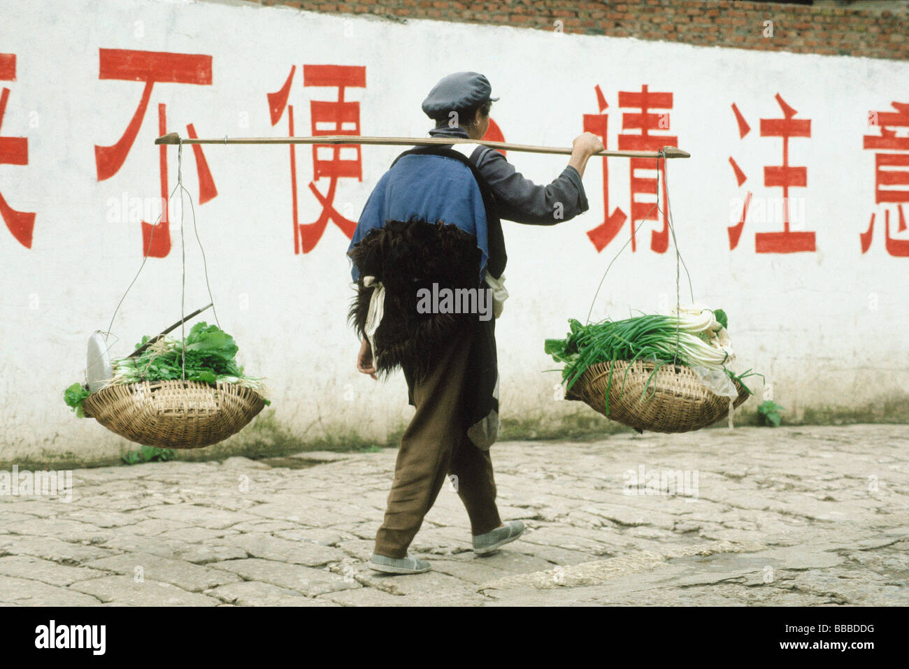 La Chine, Lijiang Naxi, homme portant des paniers de légumes Banque D'Images