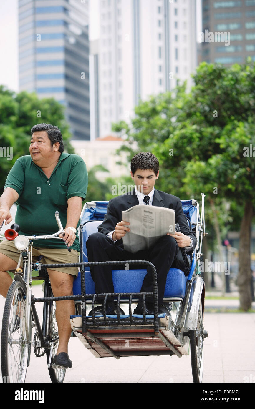 Businessman sur cyclo, reading newspaper Banque D'Images