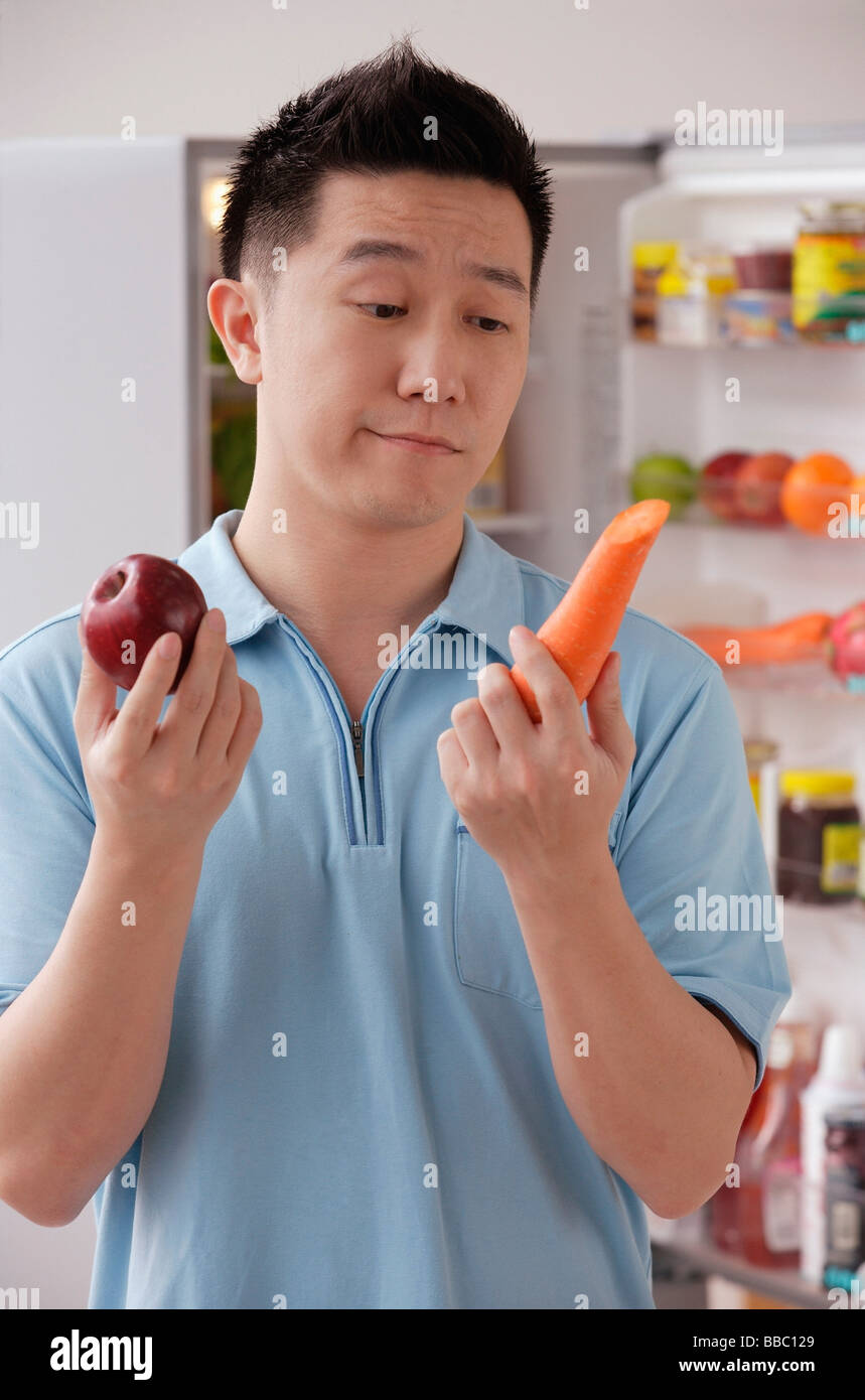 L'homme tenant une pomme et une carotte, à la frustration Banque D'Images