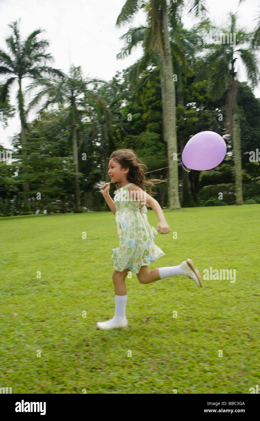 Fille courir dans le parc, purple balloon flying derrière elle Banque D'Images