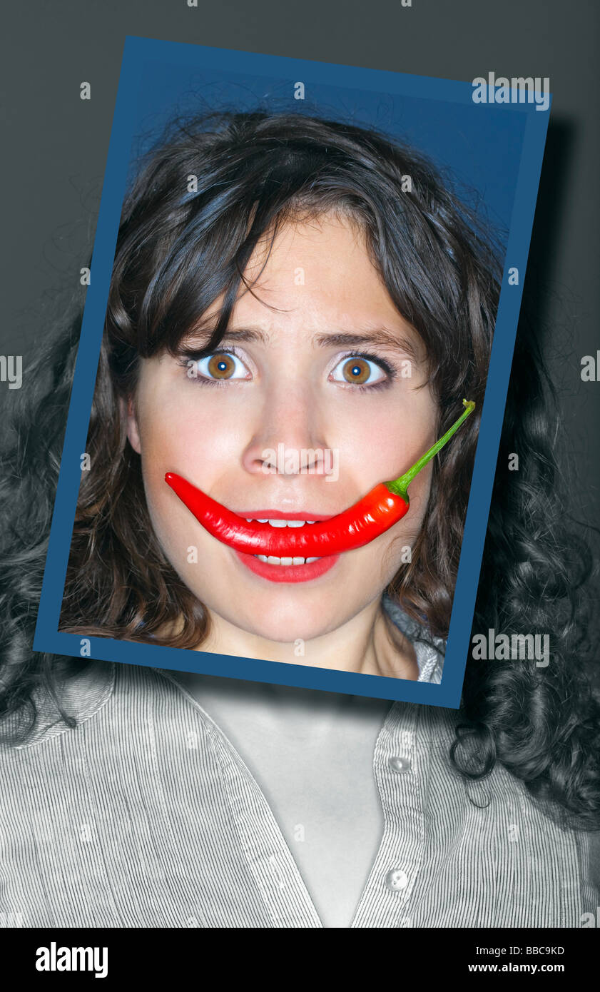 Young woman holding chili dans sa bouche encadrée face Banque D'Images