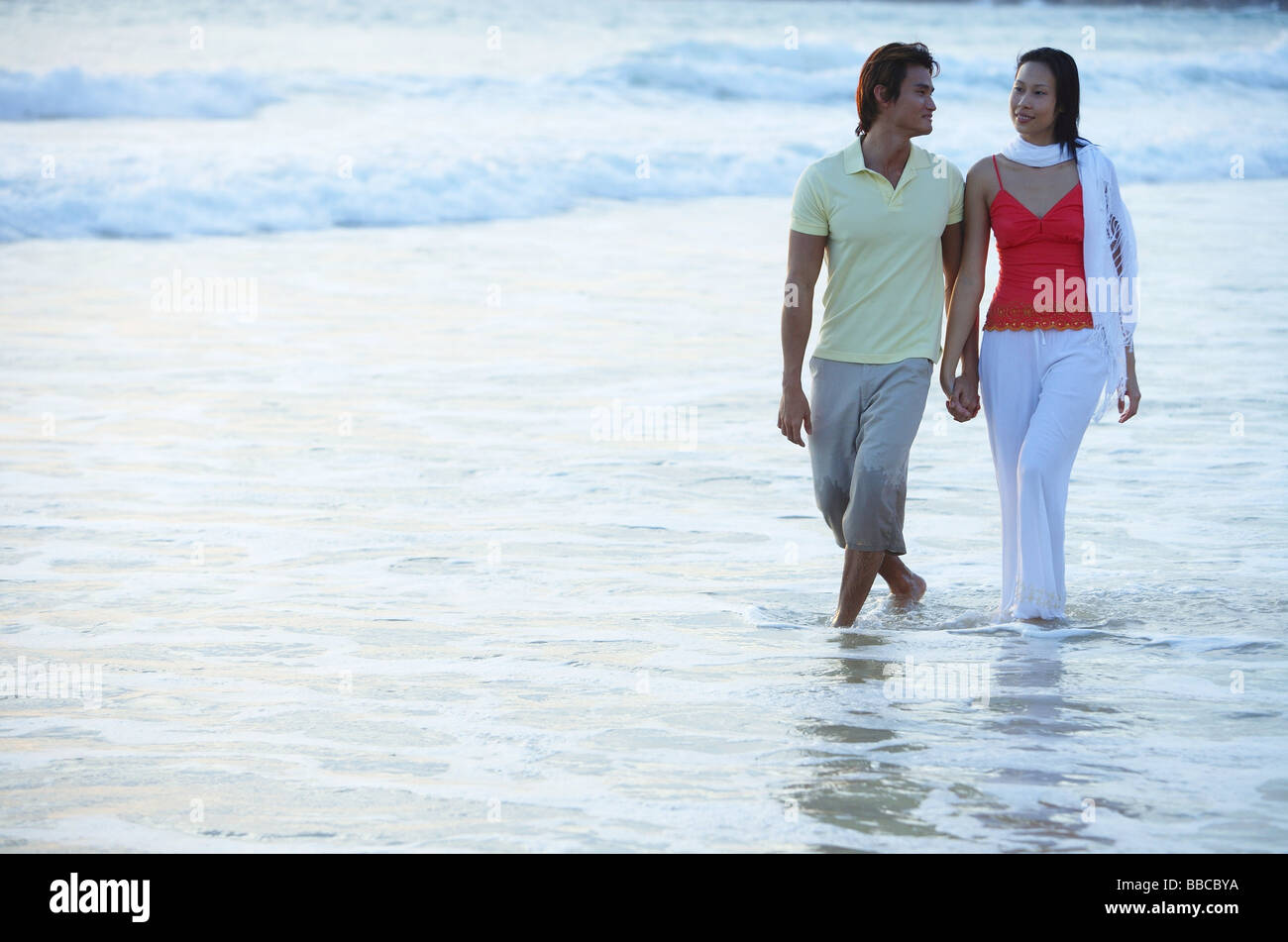 Couple walking on beach, à la cheville dans l'eau, se tenant la main Banque D'Images