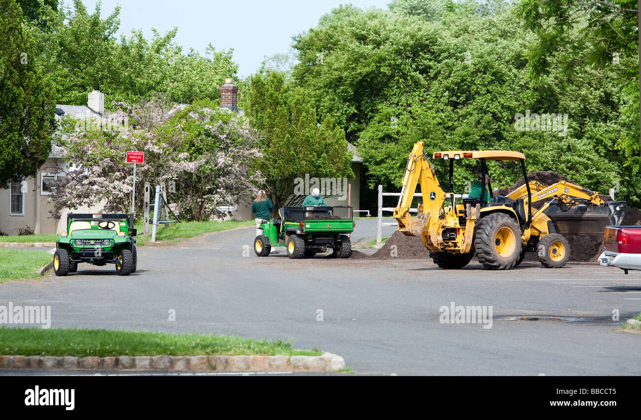 Jardiniers travaillant avec et pour l'épandage de paillis de chargement. Un tracteur John Deere jaune et varous les travailleurs et les charrettes et les VTT. Banque D'Images
