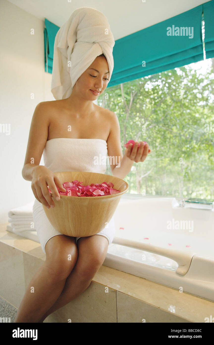 Femme dans une serviette, avec bol rempli de pétales de fleurs, assis à bord de baignoire à remous Banque D'Images