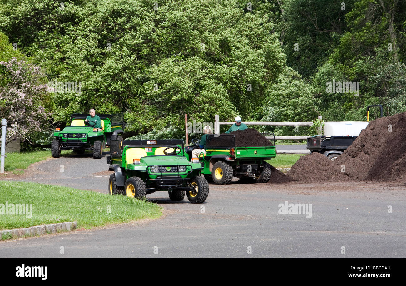 Jardiniers travaillant avec et pour l'épandage de paillis de chargement. Un tracteur John Deere jaune et varous les travailleurs et les charrettes et les VTT. Banque D'Images