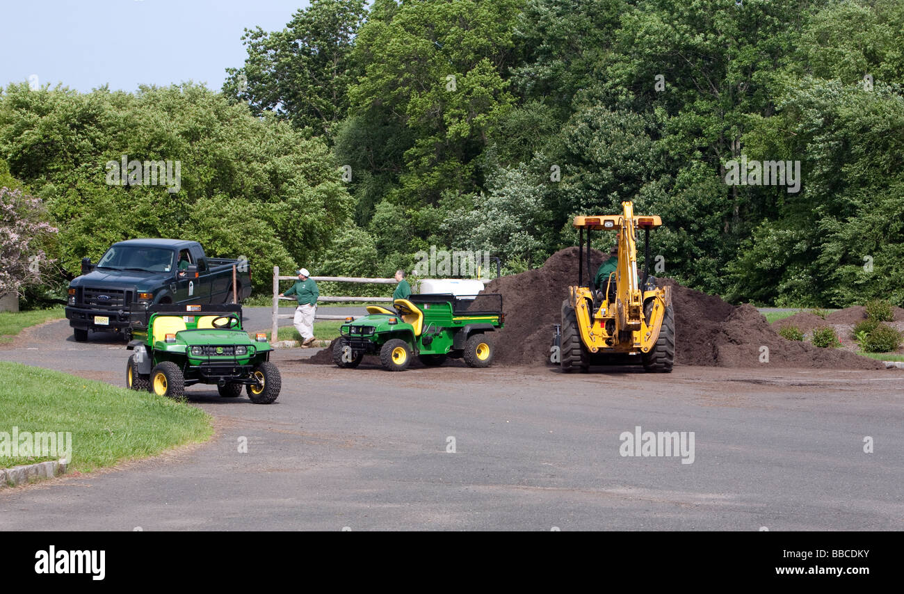 Jardiniers travaillant avec et pour l'épandage de paillis de chargement. Un tracteur John Deere jaune et varous les travailleurs et les charrettes et les VTT. Banque D'Images