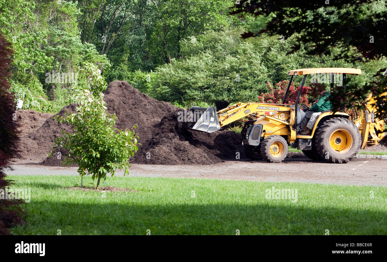 Jardiniers travaillant avec et pour l'épandage de paillis de chargement. Un tracteur John Deere jaune et varous les travailleurs et les charrettes et les VTT. Banque D'Images