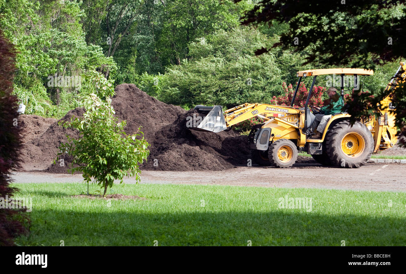 Jardiniers travaillant avec et pour l'épandage de paillis de chargement. Un tracteur John Deere jaune et varous les travailleurs et les charrettes et les VTT. Banque D'Images
