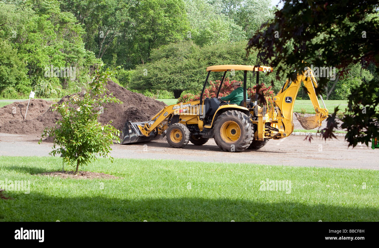 Jardiniers travaillant avec et pour l'épandage de paillis de chargement. Un tracteur John Deere jaune et varous les travailleurs et les charrettes et les VTT. Banque D'Images