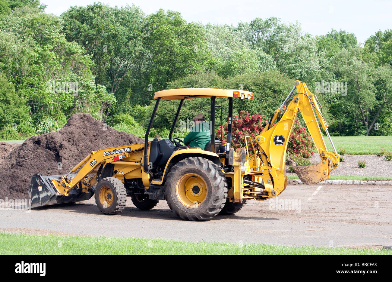 Jardiniers travaillant avec et pour l'épandage de paillis de chargement. Un tracteur John Deere jaune et varous les travailleurs et les charrettes et les VTT. Banque D'Images
