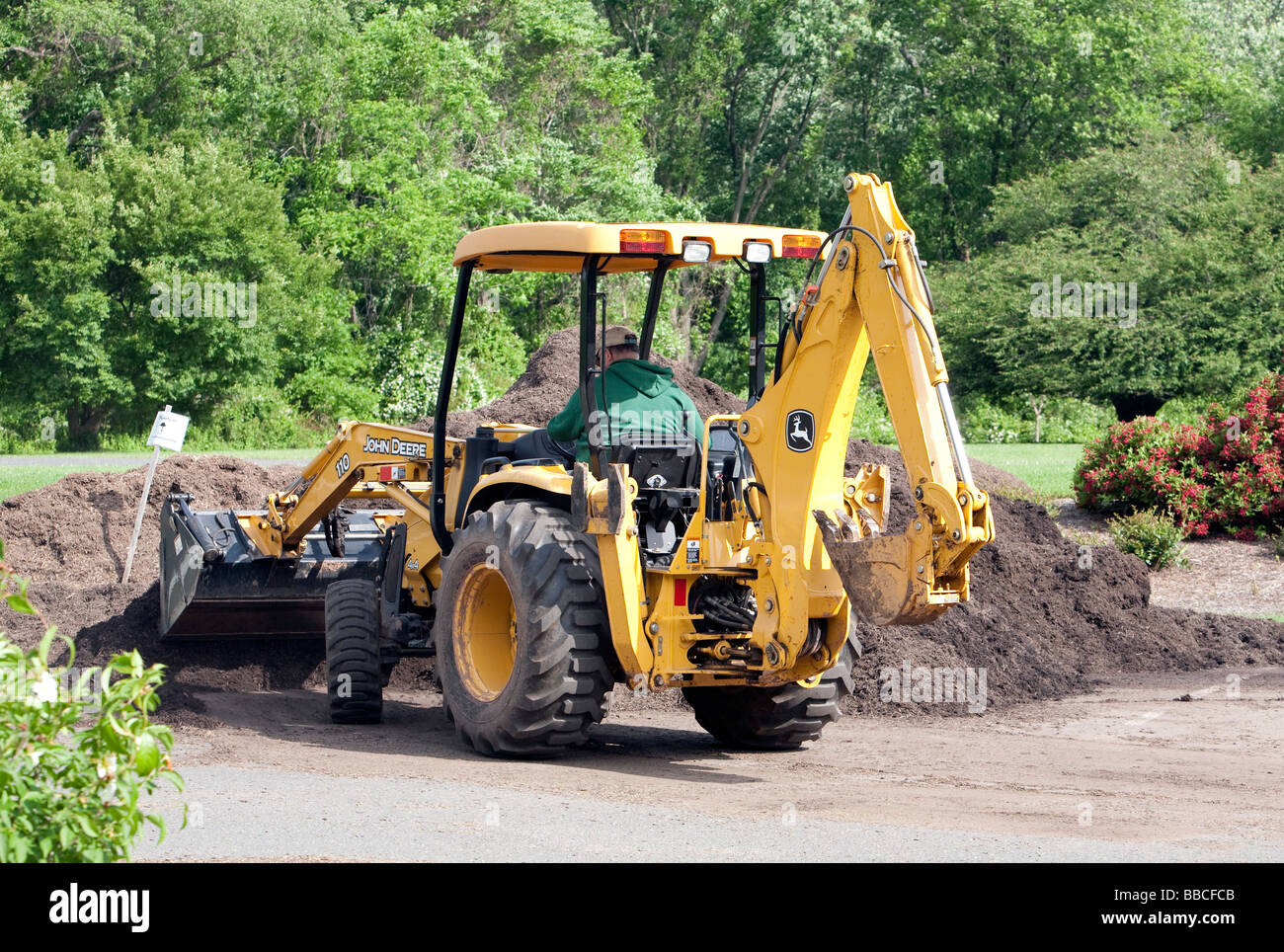 Jardiniers travaillant avec et pour l'épandage de paillis de chargement. Un tracteur John Deere jaune et varous les travailleurs et les charrettes et les VTT. Banque D'Images