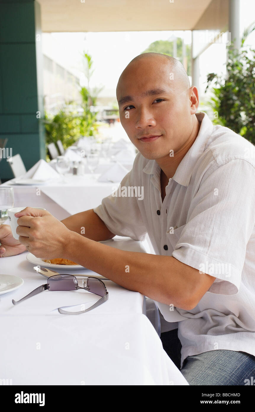 L'homme assis à table, holding cup, looking at camera Banque D'Images