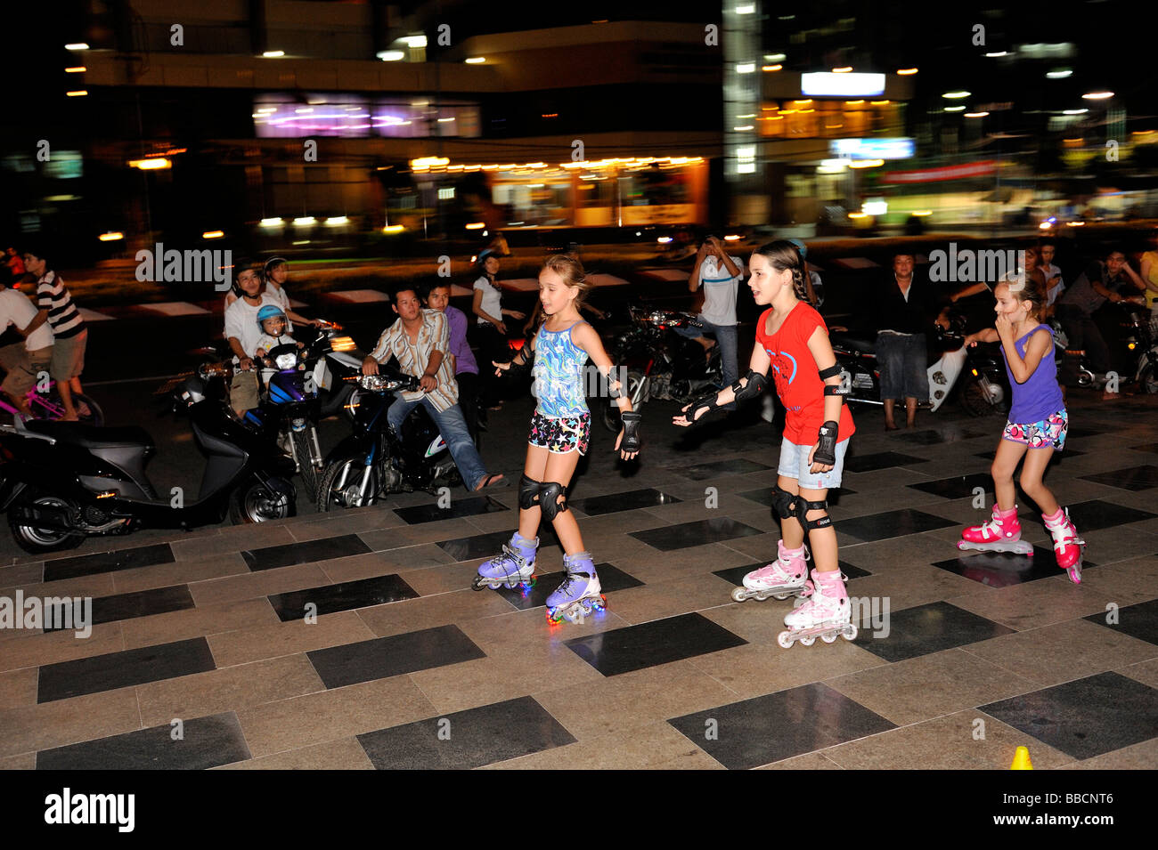 Trois enfants (10 ans, 8 ans, 7 ans) Cours de patinage spectateurs en bordure de rue la nuit. Vung Tau, Vietnam Banque D'Images