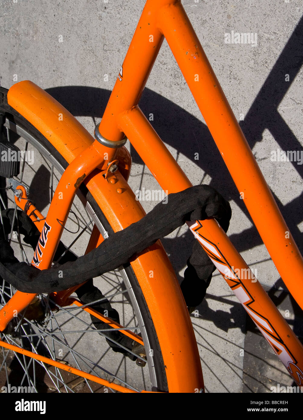 Le passage de roue avant et le cadre d'une orange location jette une ombre sur un mur Banque D'Images