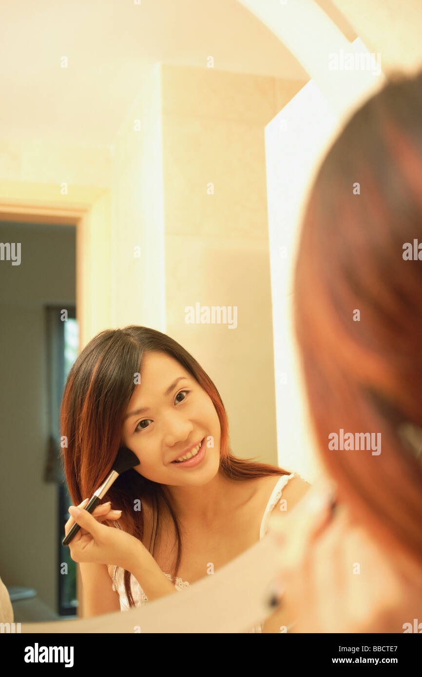 Woman putting on mascara, à la recherche de miroir, smiling Banque D'Images