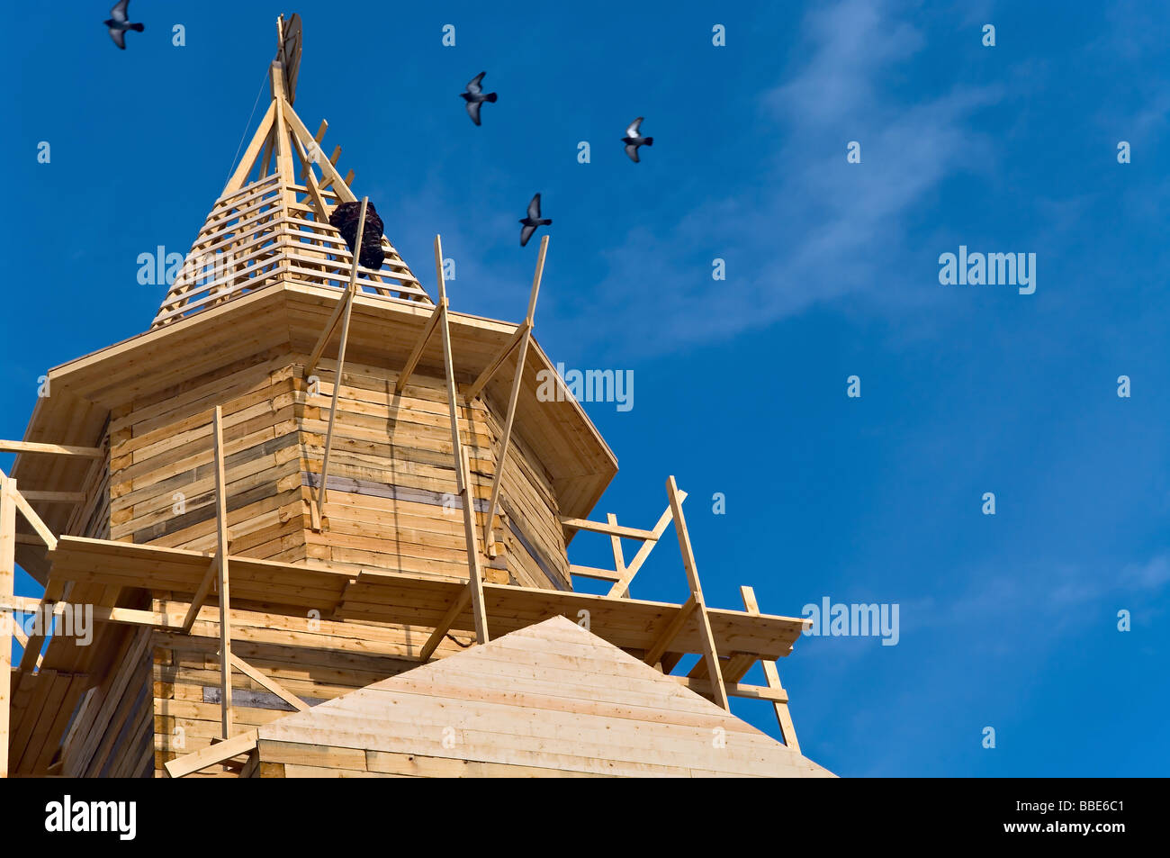 Fragment de l'église en bois à partir de poutres en construction sur le fond de ciel bleu. L'homme sur le toit et des tourterelles autour Banque D'Images