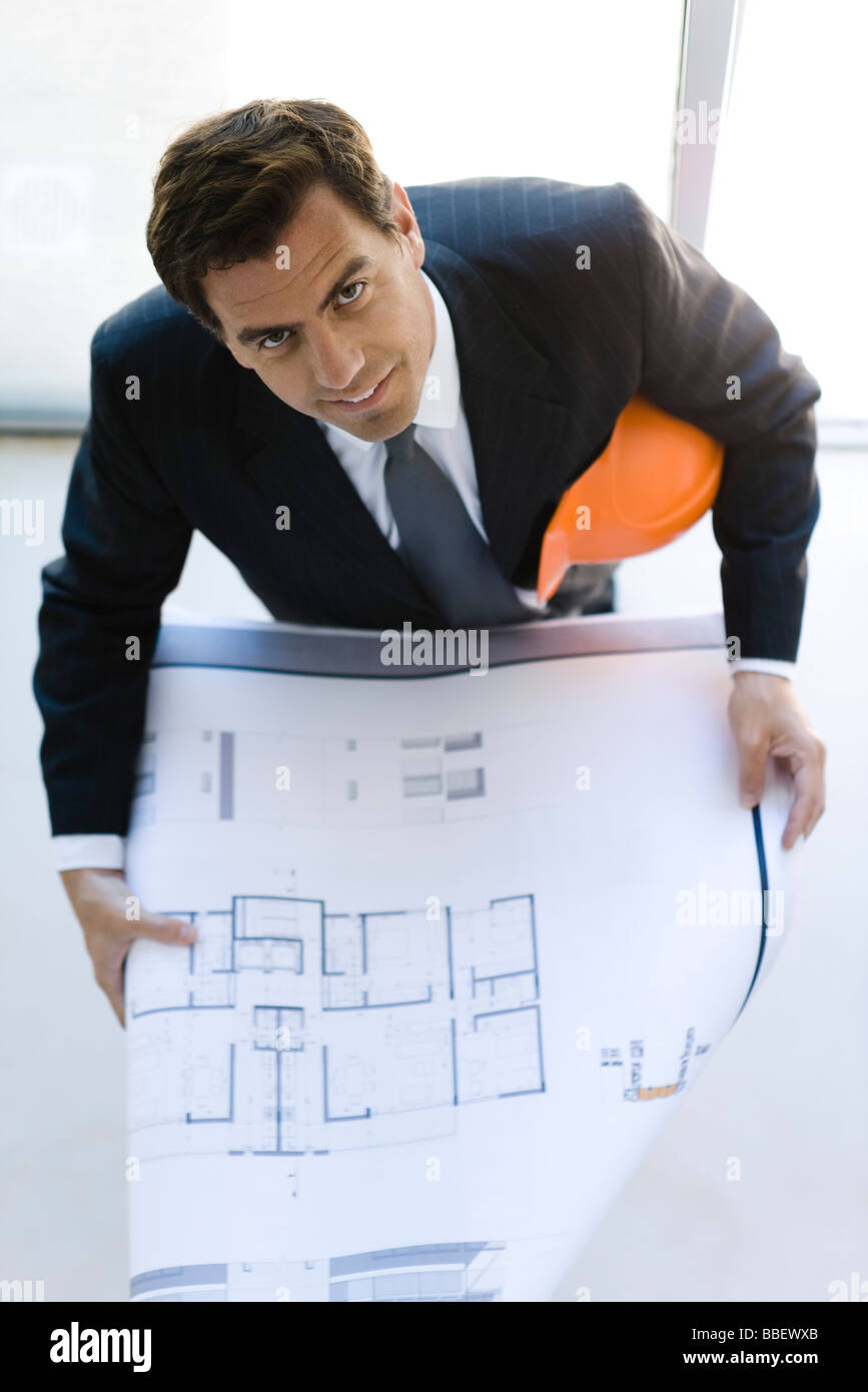 Man in suit holding blueprints looking up at camera Banque D'Images