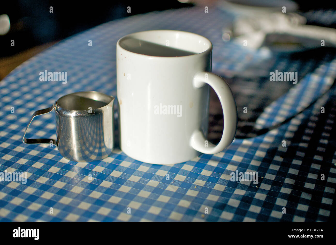 Une tasse de thé blanc porcelaine et petit pot à lait en acier inoxydable  sur un fond bleu et blanc tapis de table dans un café de transport  traditionnel anglais Photo Stock -