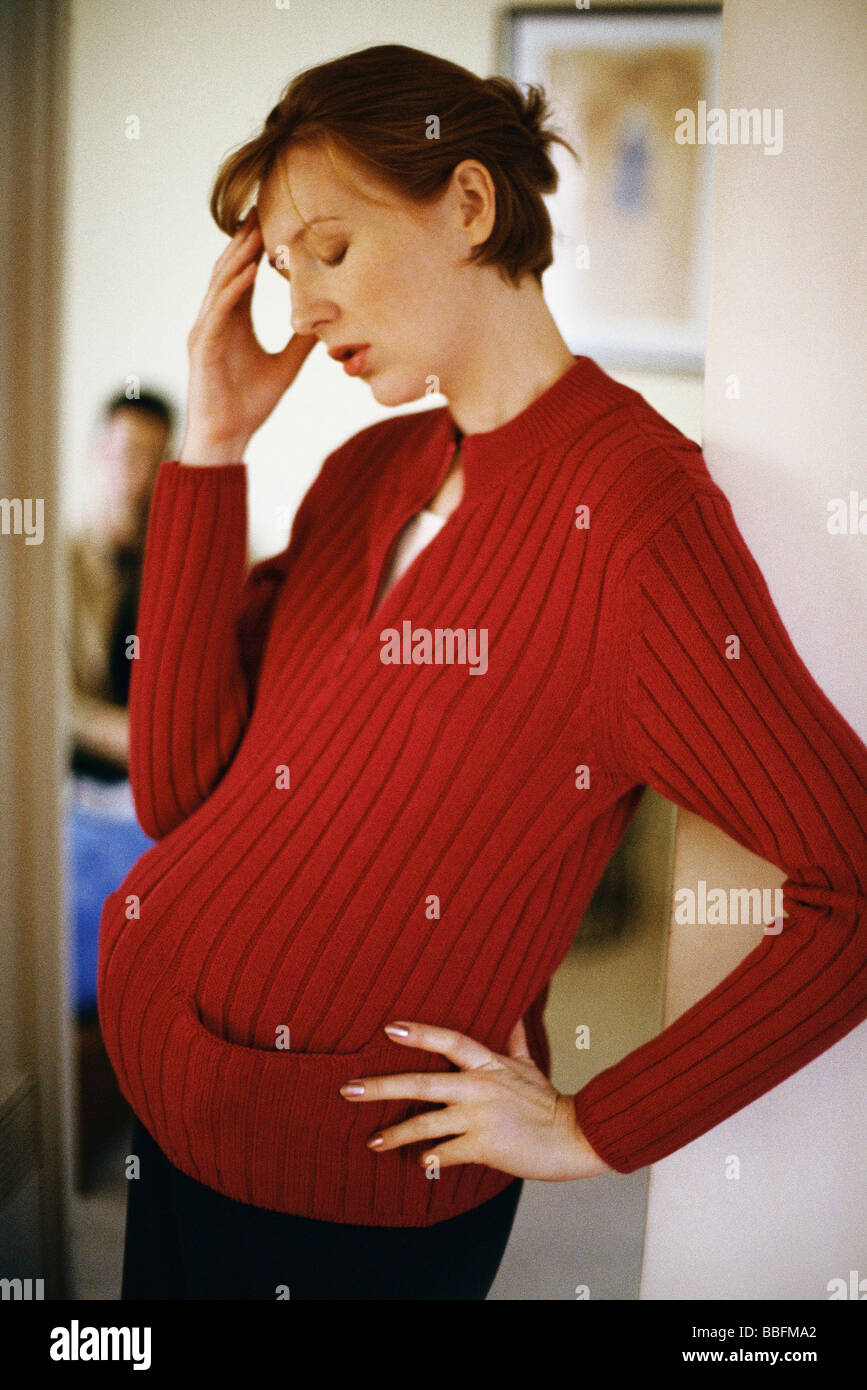Pregnant woman holding head, l'homme en arrière-plan Banque D'Images