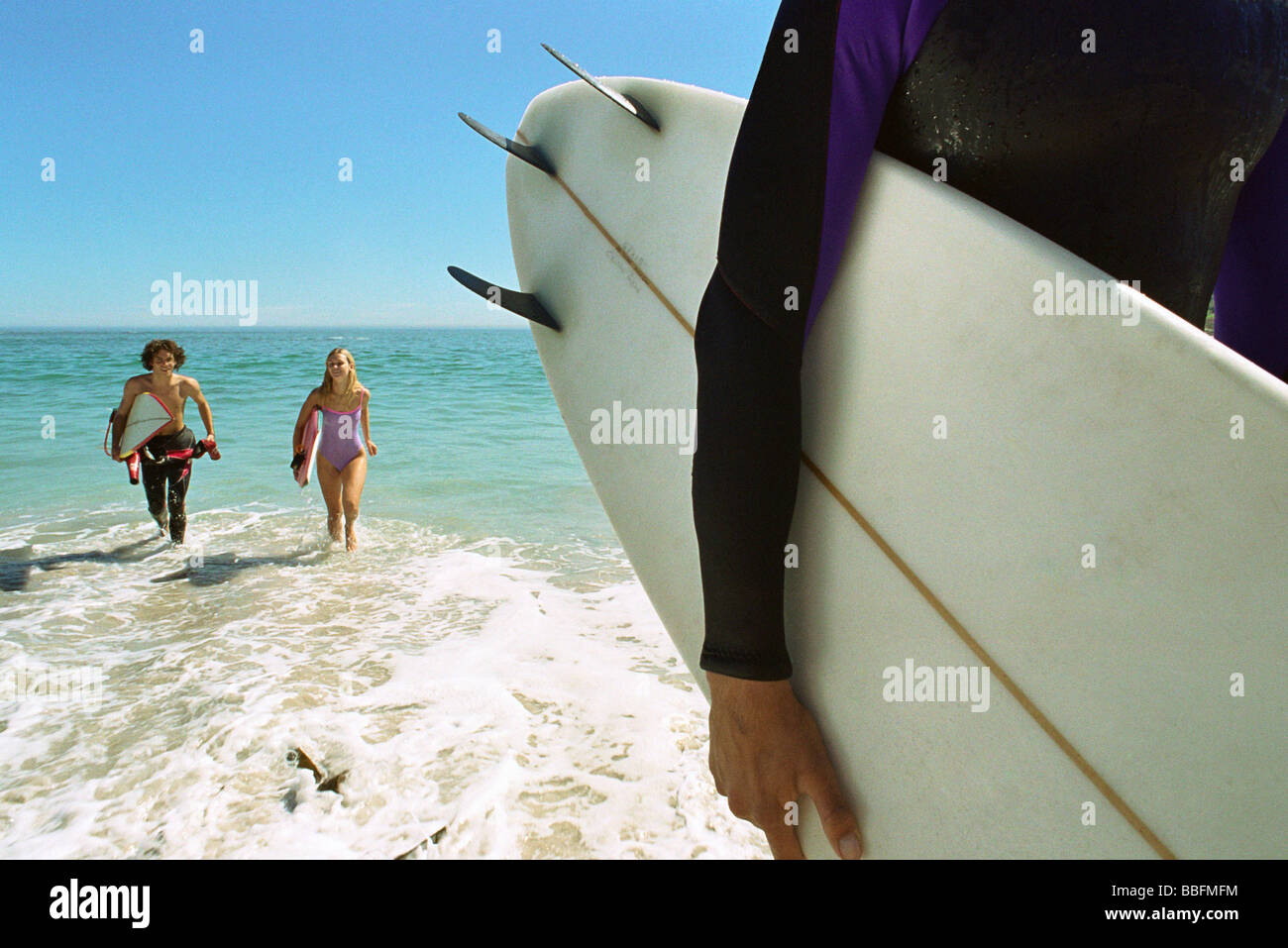 Surfer carrying board sous le bras, un couple sortant d'eau ensemble Banque D'Images