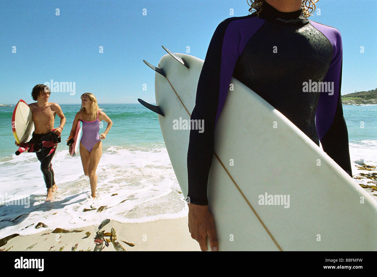 Surfer carrying board sous le bras, un couple sortant d'eau ensemble Banque D'Images