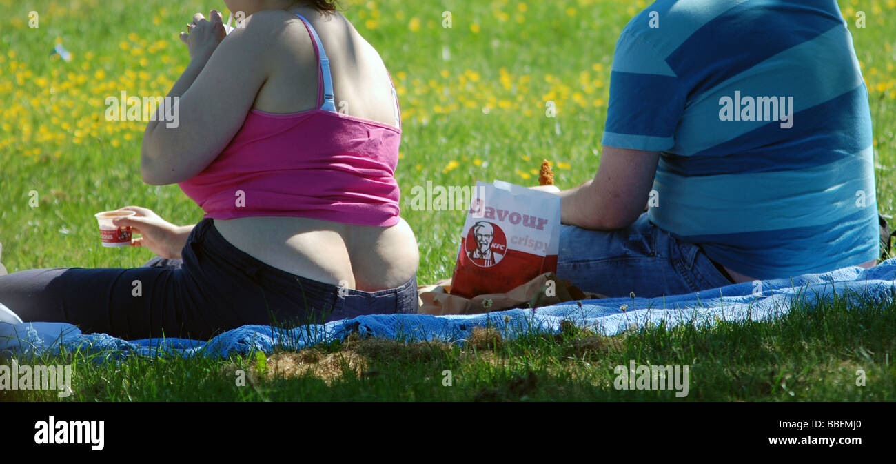 L'excès de l'homme et la femme : un couple obèse mangeant un KFC au soleil. Banque D'Images