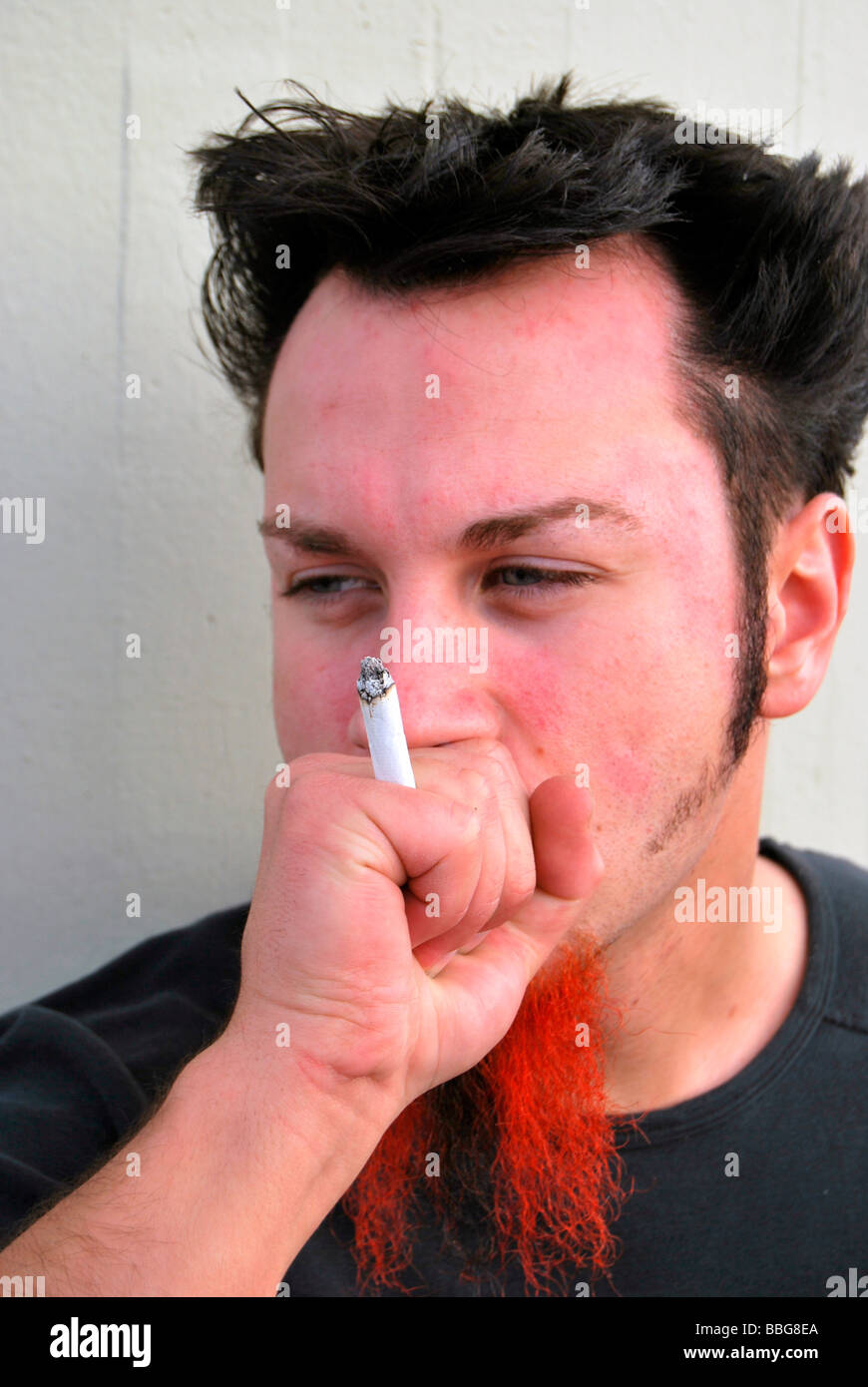 Fumeurs mauvaise herbe, jeune homme avec barbe rouge-noir fumer un joint, cigarette roulée à la main Banque D'Images