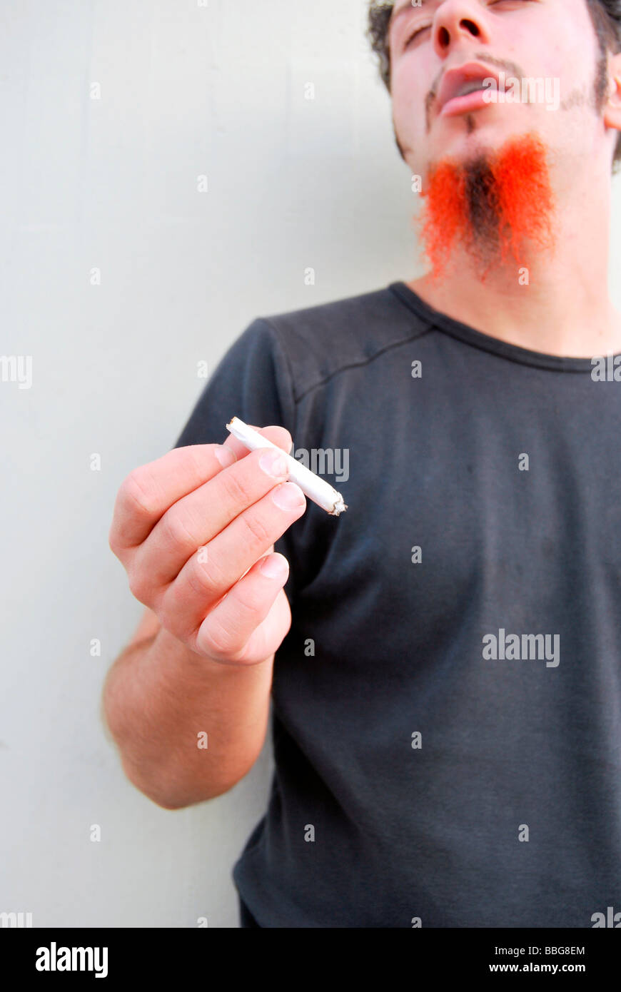 Médicaments, jeune homme avec barbe rouge-noir tenant un joint, cigarette roulée à la main Banque D'Images