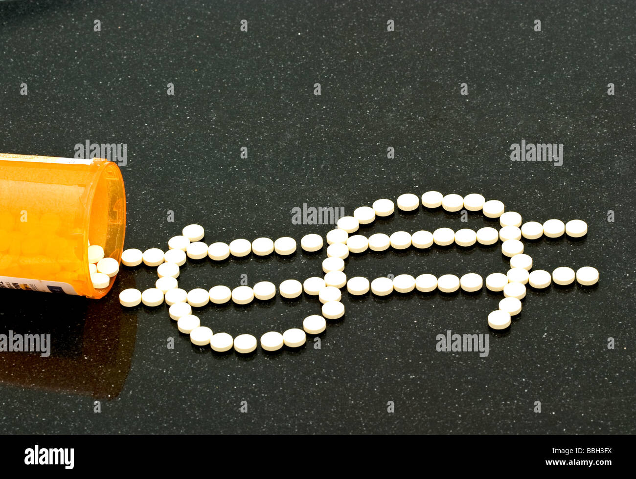 Les petites pilules blanches en forme d'un signe dollar à côté d'une bouteille de prescription d'orange partiellement rempli de comprimés Banque D'Images