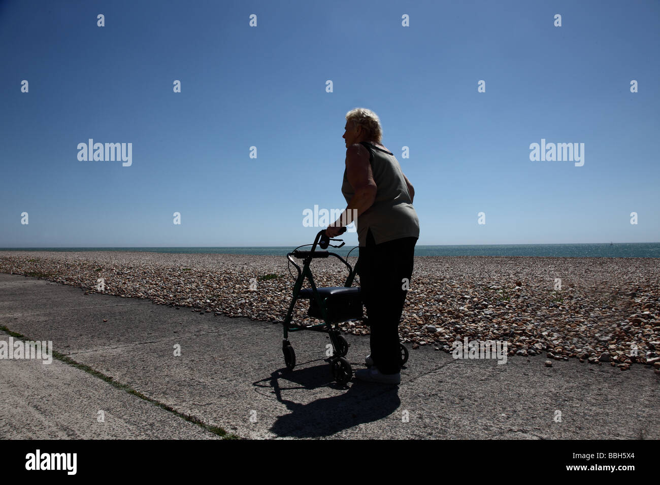 Femme âgée marche loin de la caméra le long de la plage dans le soleil couchant Banque D'Images