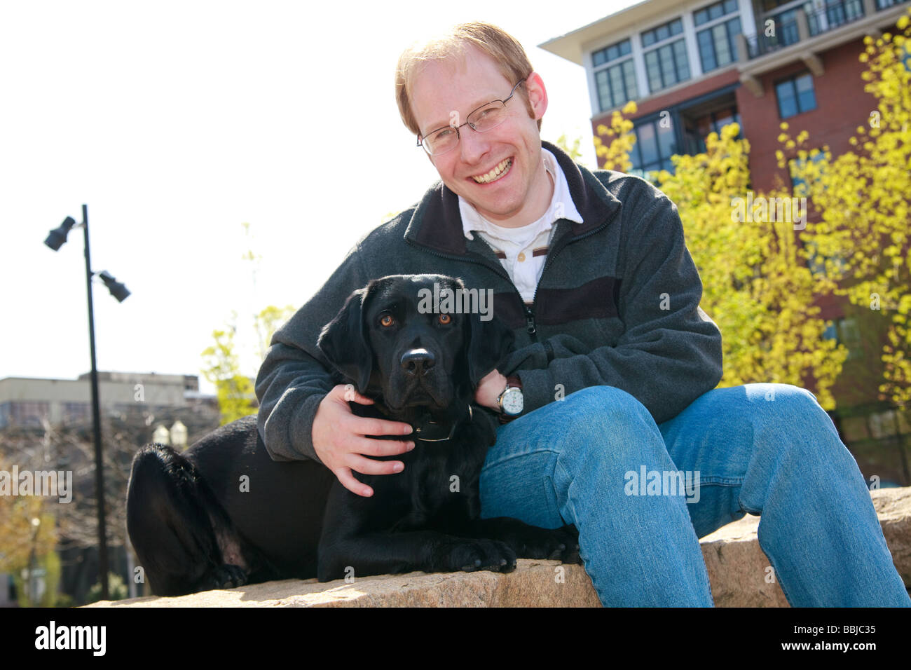 Jeune homme blanc avec chien labrador noir garde d'animaux à l'extérieur en milieu urbain pour les condos du parc avec en arrière-plan. Banque D'Images