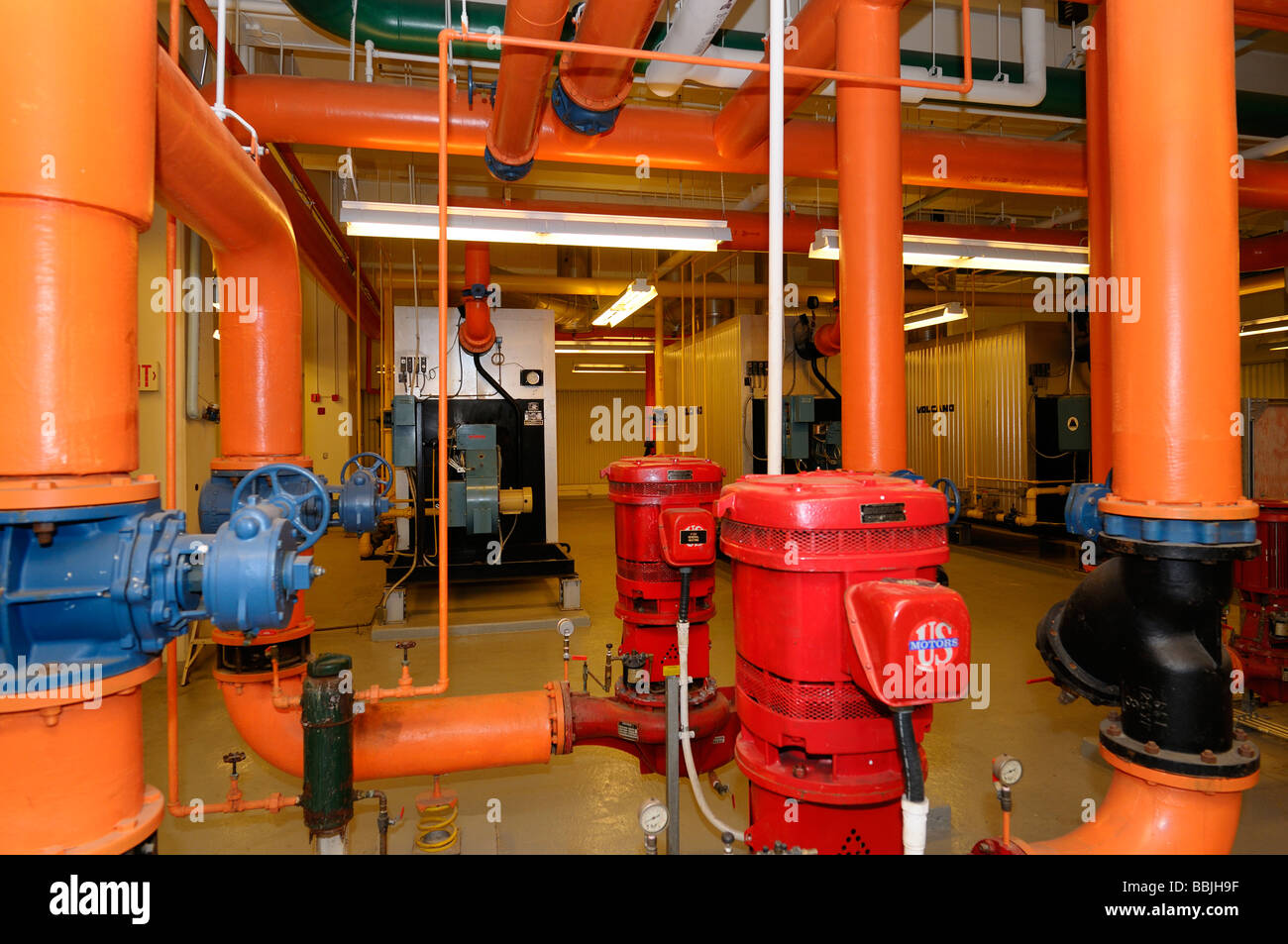 Rangée de fours et conduites d'eau chaude orange peint dans la chaufferie d'un immeuble de bureaux de grande hauteur Banque D'Images