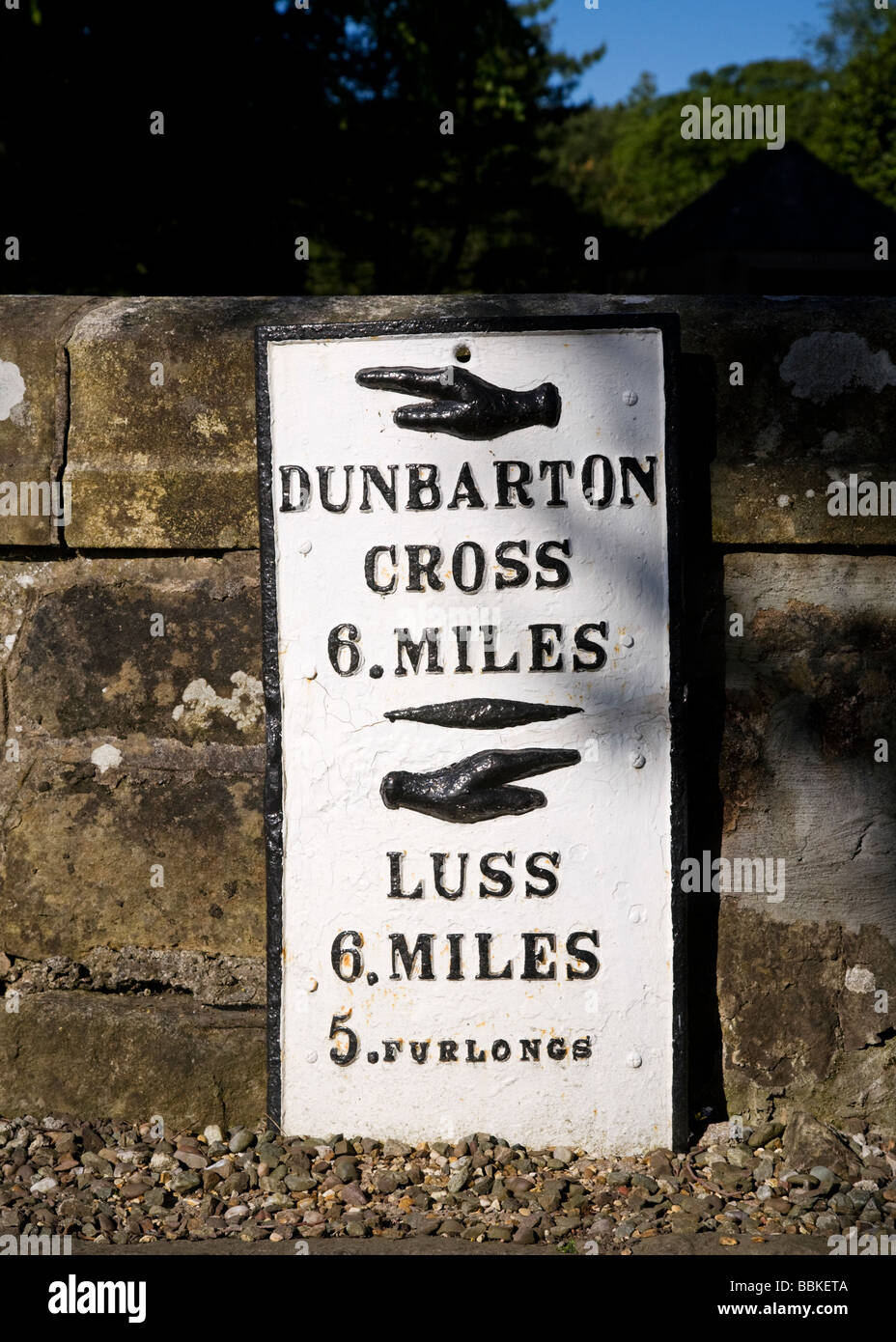 Un vieux panneau routier sur un mur indiquant la distance entre Dunbarton et Luss, Loch Lomond, Ecosse. Banque D'Images