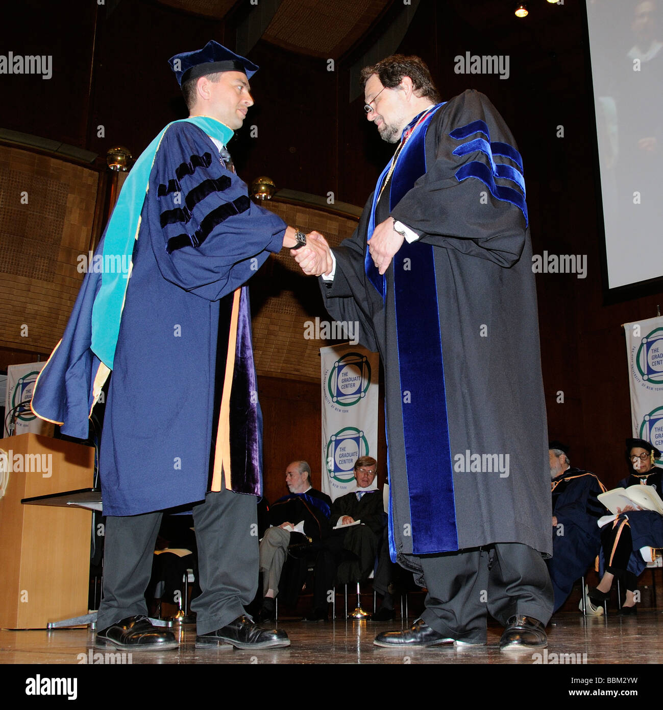 Cérémonie de remise de diplômes d'études supérieures d'hommes wearing cap and gown avec les responsables de l'Université de la scène Banque D'Images