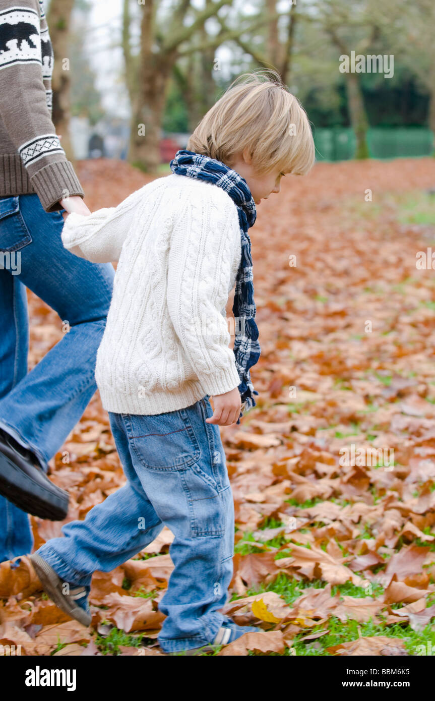 Jeune garçon marchant à travers les feuilles d'automne holding woman's hand, Vancouver, Colombie-Britannique Banque D'Images