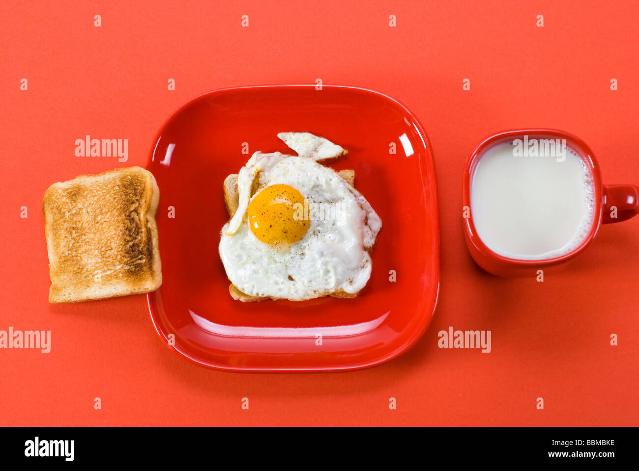 Le petit-déjeuner, tasse de lait, pain grillé, œuf frit assaisonné de sel et de poivre sur la vaisselle rouge Banque D'Images