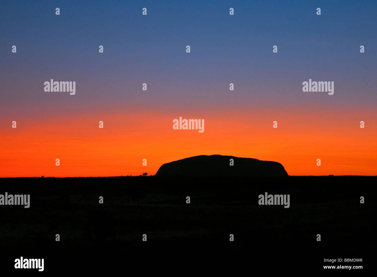 L'Australie, Territoire du Nord. Avant le lever du soleil sur Uluru, ou Ayres Rock est découpé sur un magnifique ciel orange ou rouge sang Banque D'Images
