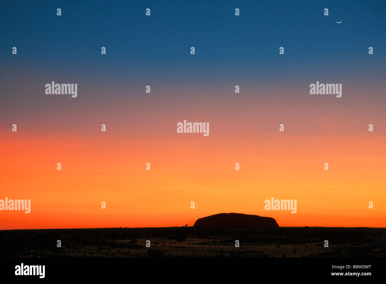 L'Australie, Territoire du Nord. Avant le lever du soleil sur Uluru, ou Ayres Rock est découpé sur un magnifique ciel orange ou rouge sang Banque D'Images