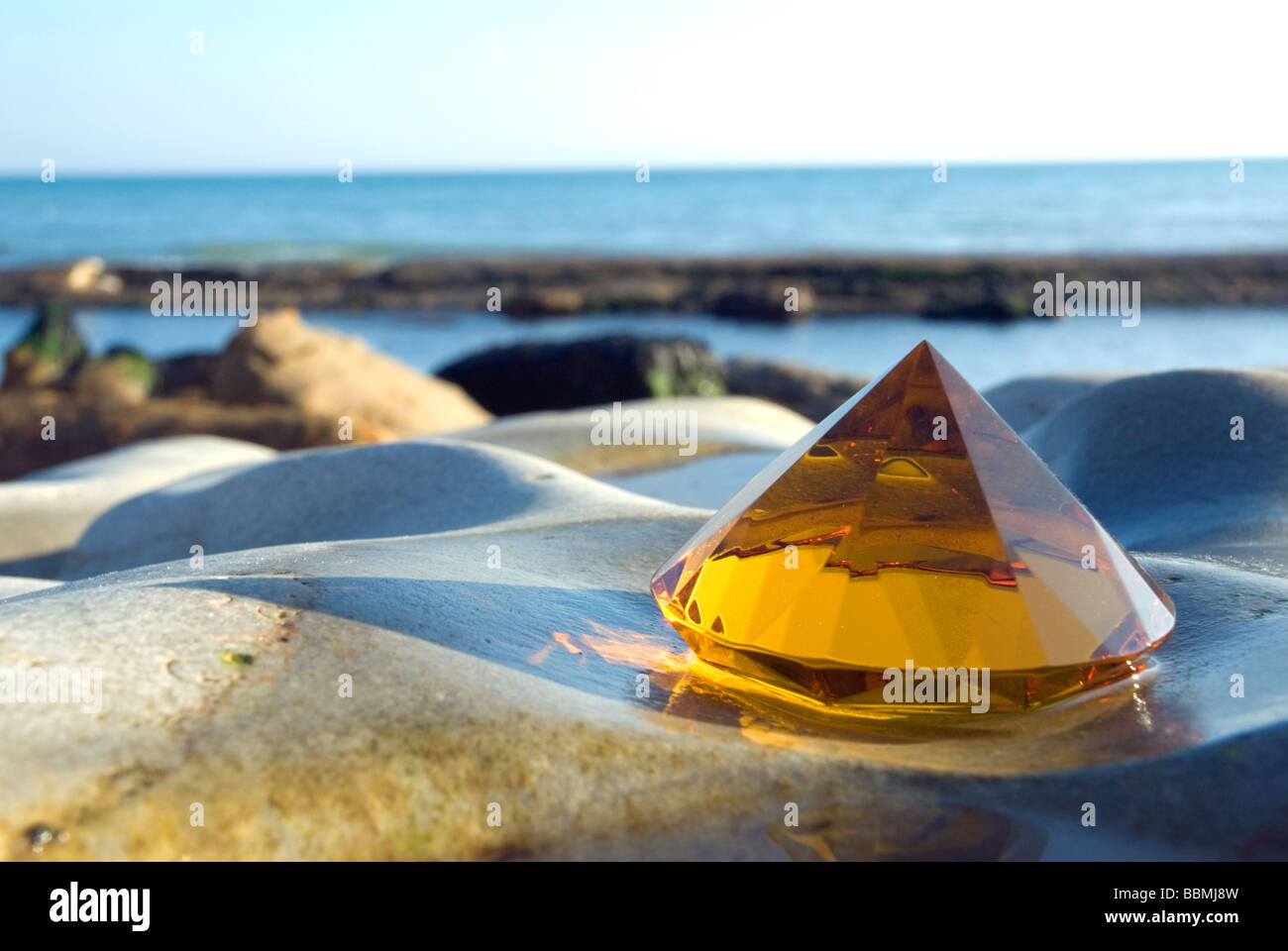 Pyramide en verre ambré sur rock avec l'eau de mer chauffée Banque D'Images
