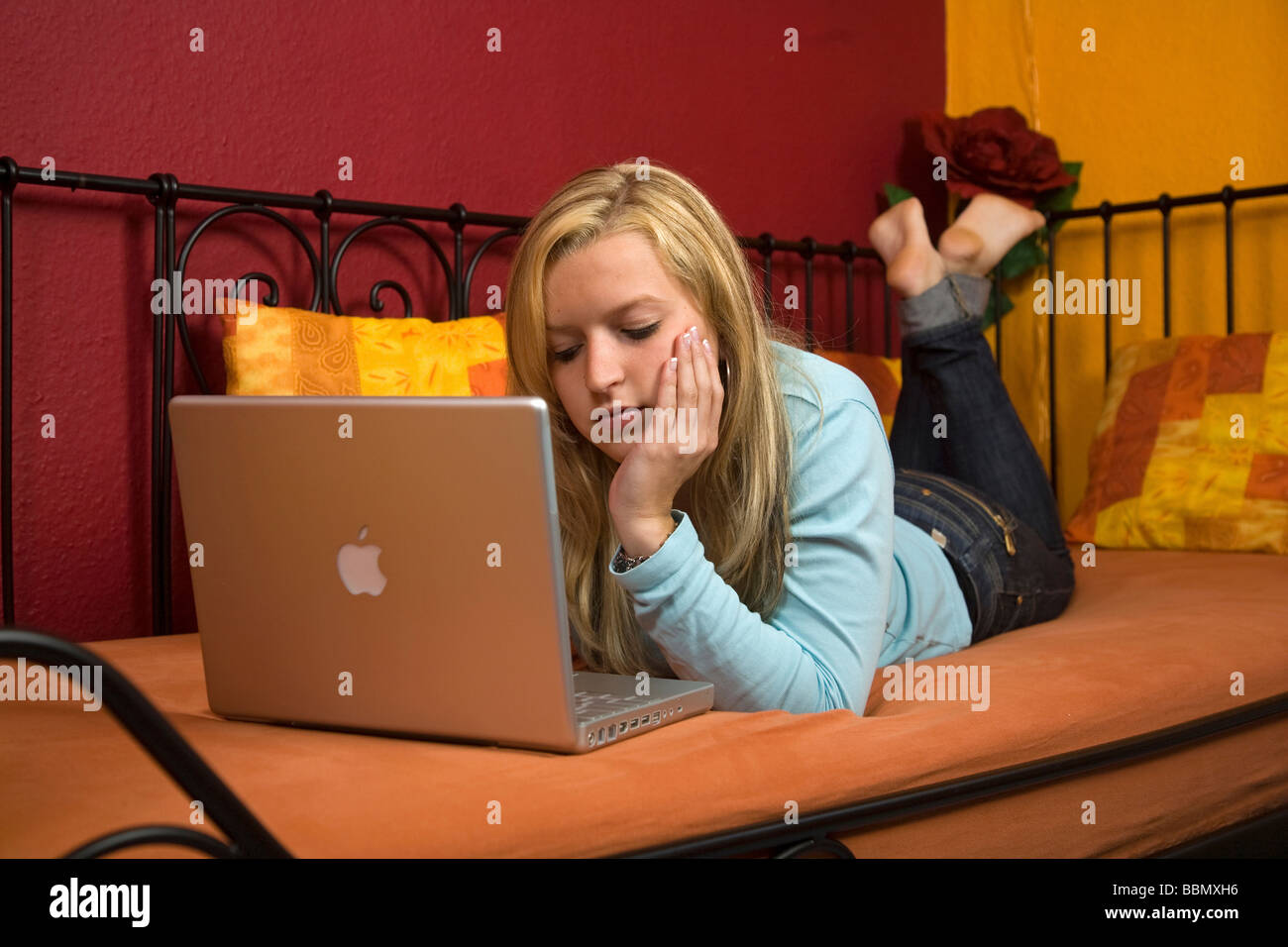 Young woman lying on a bed travaillant sur un ordinateur portable Banque D'Images