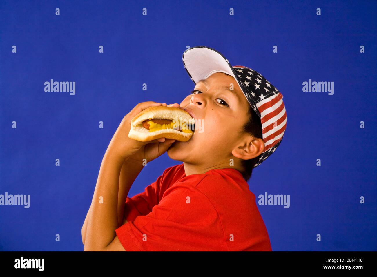 Portrait of happy young woman wearing Juillet 4ème étoile stripes hat eating hotdog décoration USA © Myrleen Pearson Banque D'Images