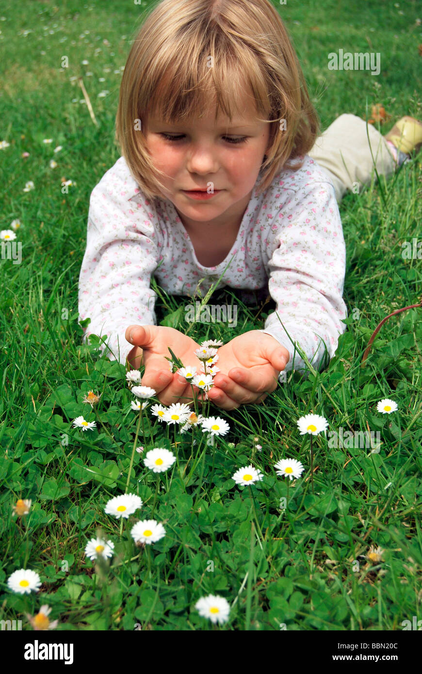 Fille, 5 ans, allongé sur une prairie avec pâquerettes (Bellis perennis) et la tenue des fleurs dans ses mains Banque D'Images