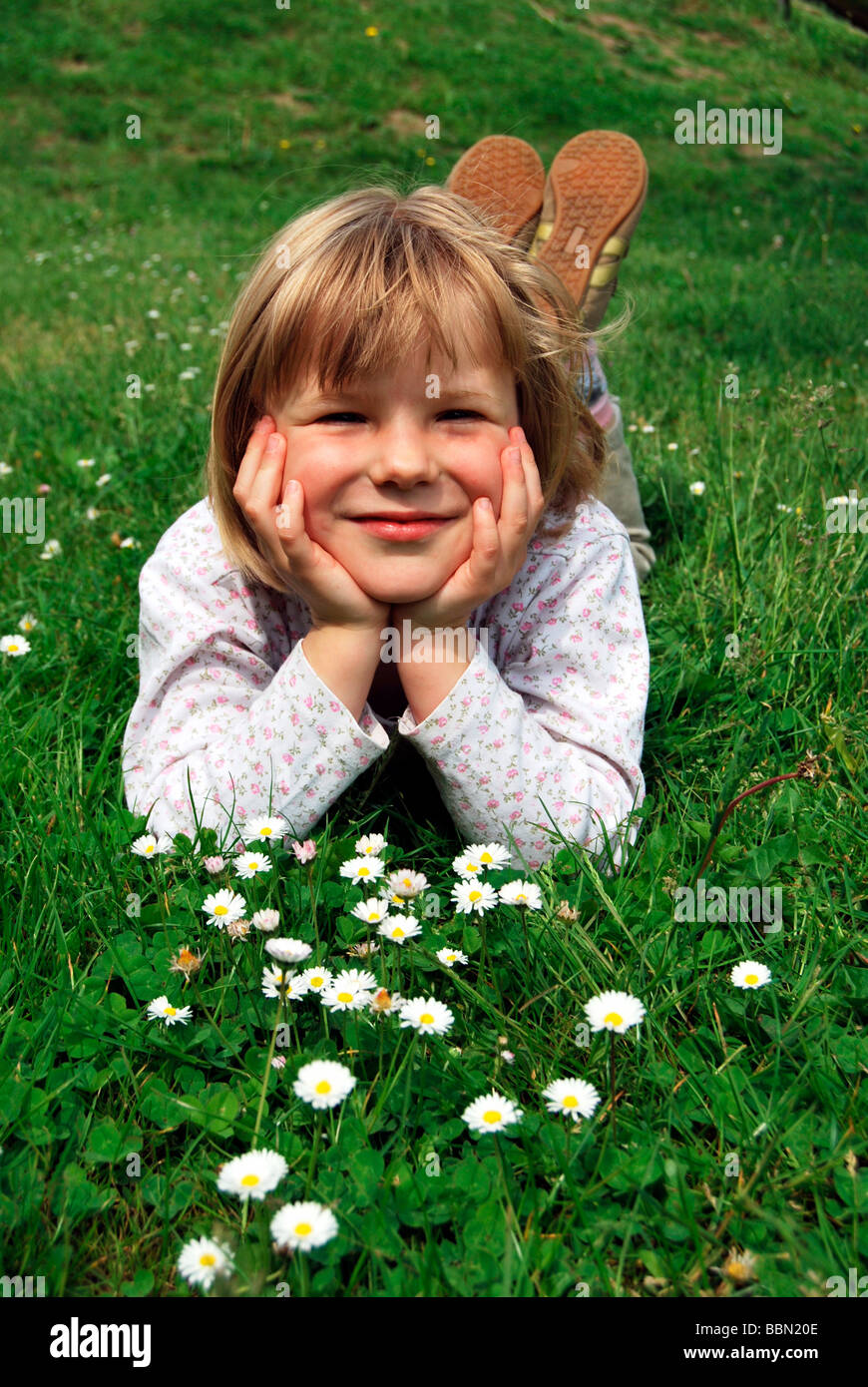 Fille, 5 ans, allongé sur une prairie avec pâquerettes (Bellis perennis) Banque D'Images