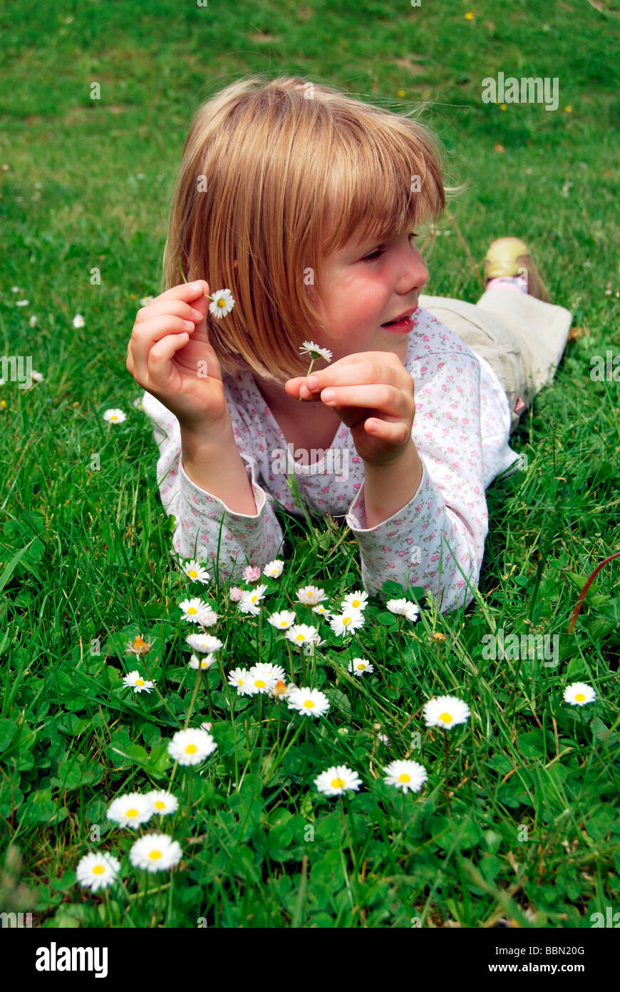 Fille, 5 ans, allongé sur une prairie avec pâquerettes (Bellis perennis) et la tenue des fleurs dans ses mains Banque D'Images