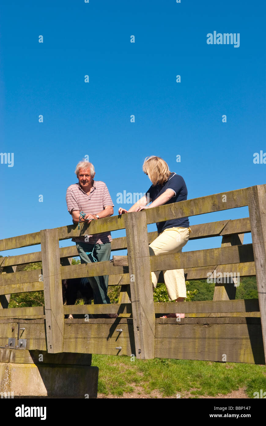 Une femme dans la trentaine et un homme septuagénaire, parler debout sur un pont de la campagne au printemps au Royaume-Uni Banque D'Images
