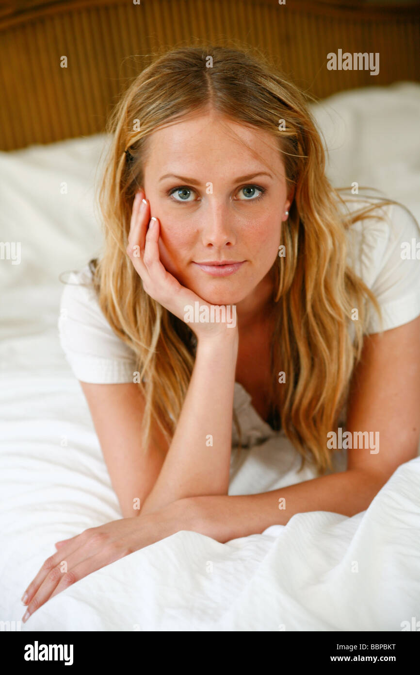 Young Caucasian woman assise ou couchée sur un lit blanc. Banque D'Images