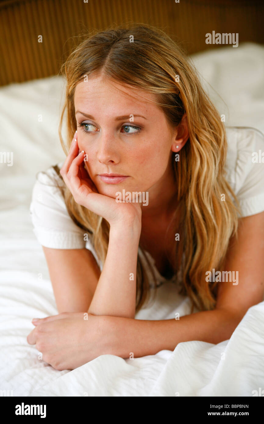 Young Caucasian woman assise ou couchée sur un lit blanc. Banque D'Images